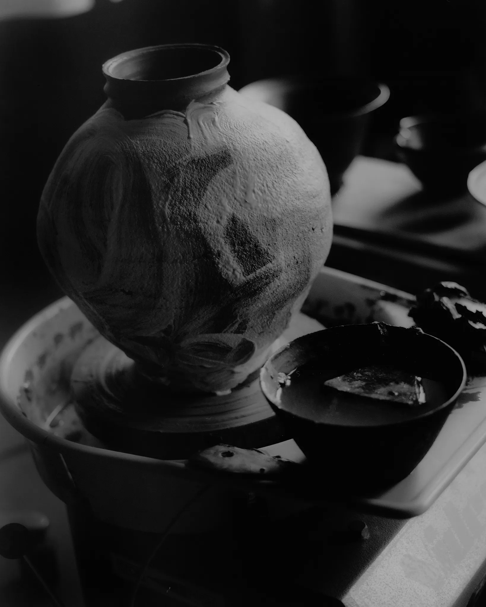 A freshly thrown vessel resting on the wheel, and a portrait in the studio