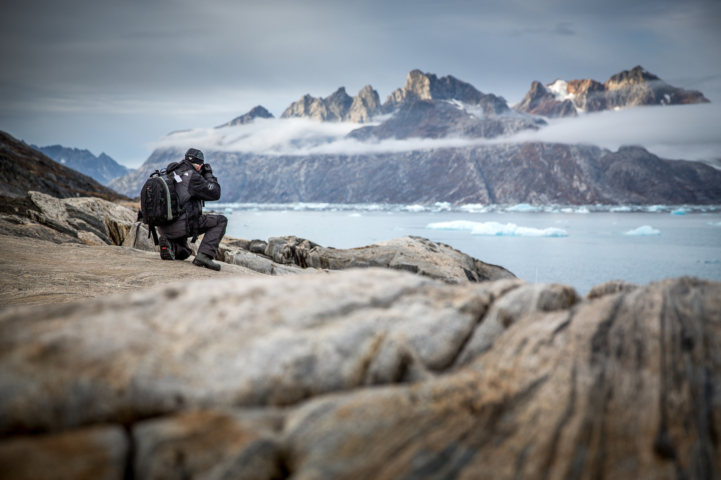 A photographer shooting rugged mountain peaks near Sermiligaaq in East Greenland. Photo by Mads Pihl - Visit Greenland