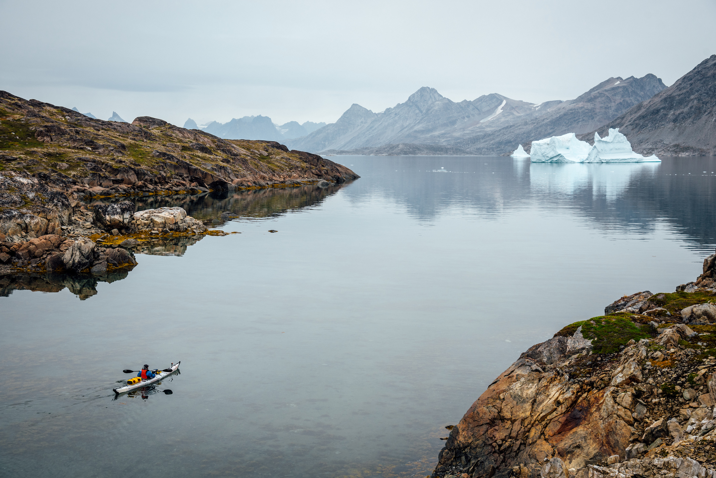 Paddler leaves camp/shore with iceberg in back, looking North, Between Kulusuk and Kuummiut. Photo - Chris B. Lee, Visit Greenland